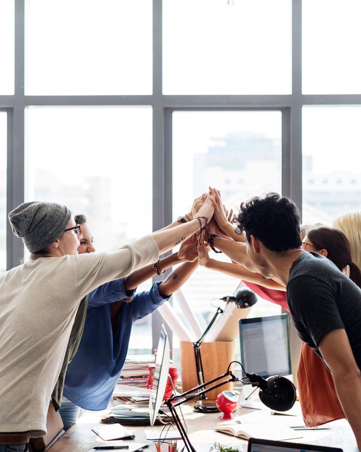 Image of a group of people coming together to high five over a table at work.