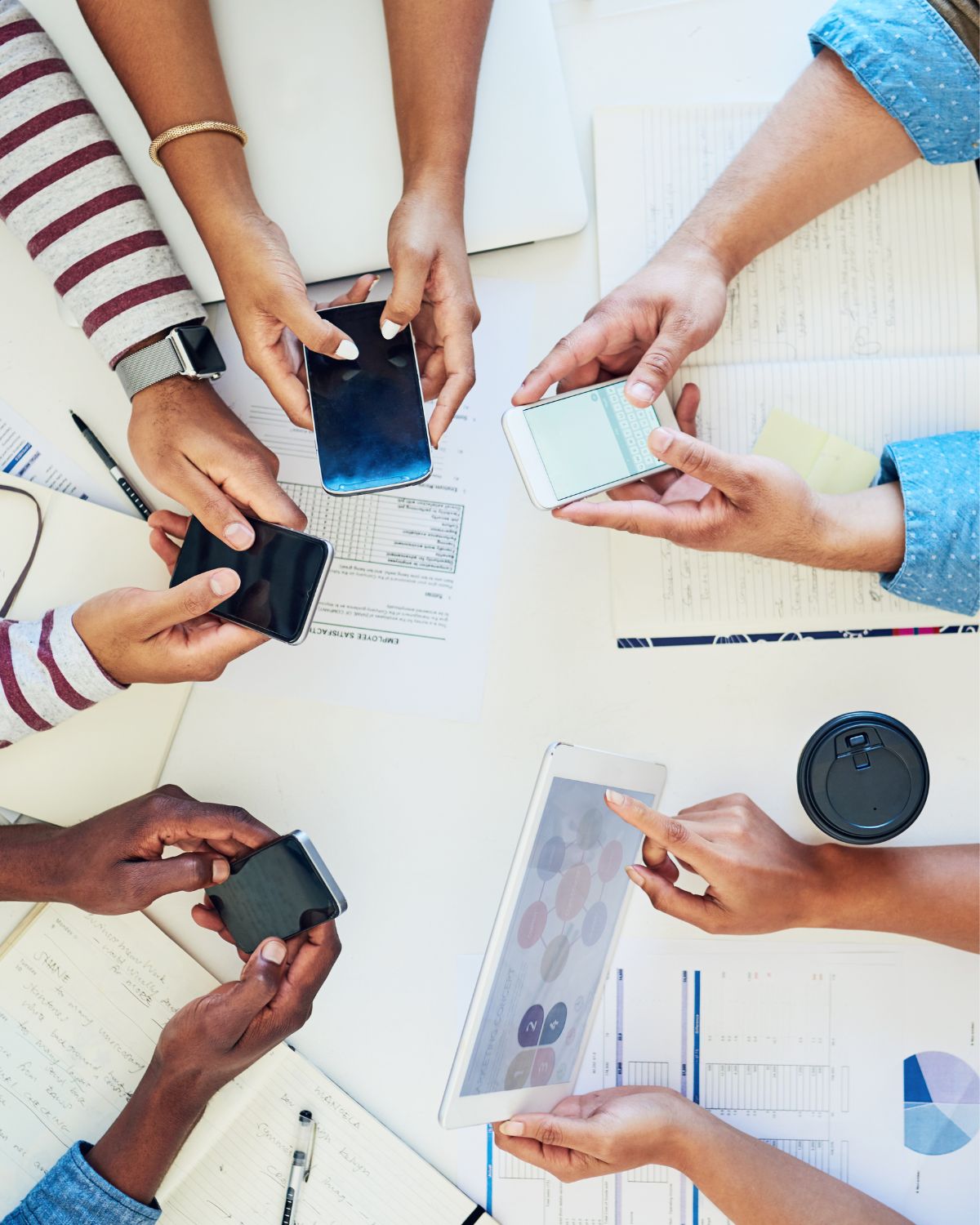 A group of people gathered around a table all holding phones.